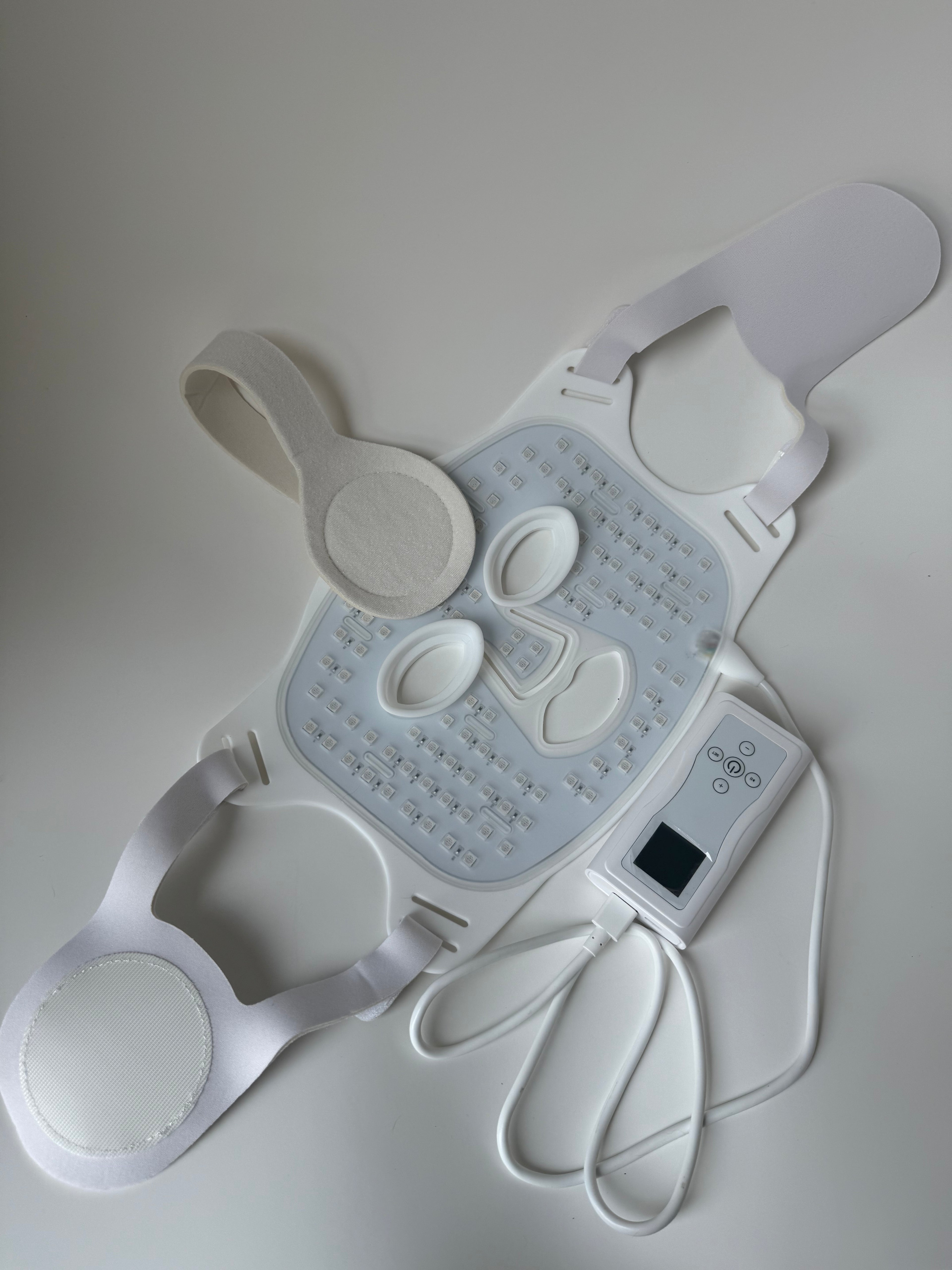 LED red light therapy face mask kit with controller, adjustable straps, and USB charger laid out on a white surface
