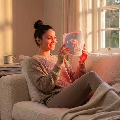 Woman sitting on a couch holding a pink face mask with a cartoon design.