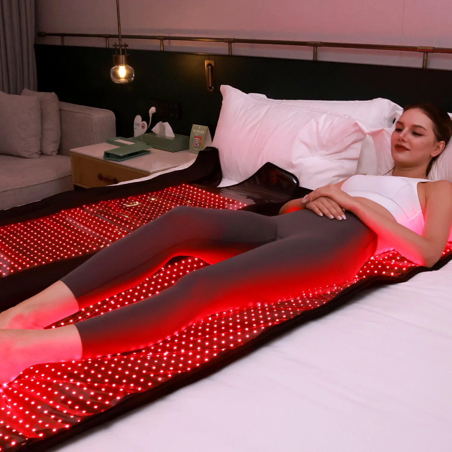 Woman lying on a bed with a red LED blanket in a cozy bedroom setting.