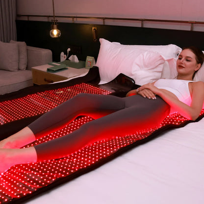 Woman lying on a bed with a red LED blanket in a cozy bedroom setting.