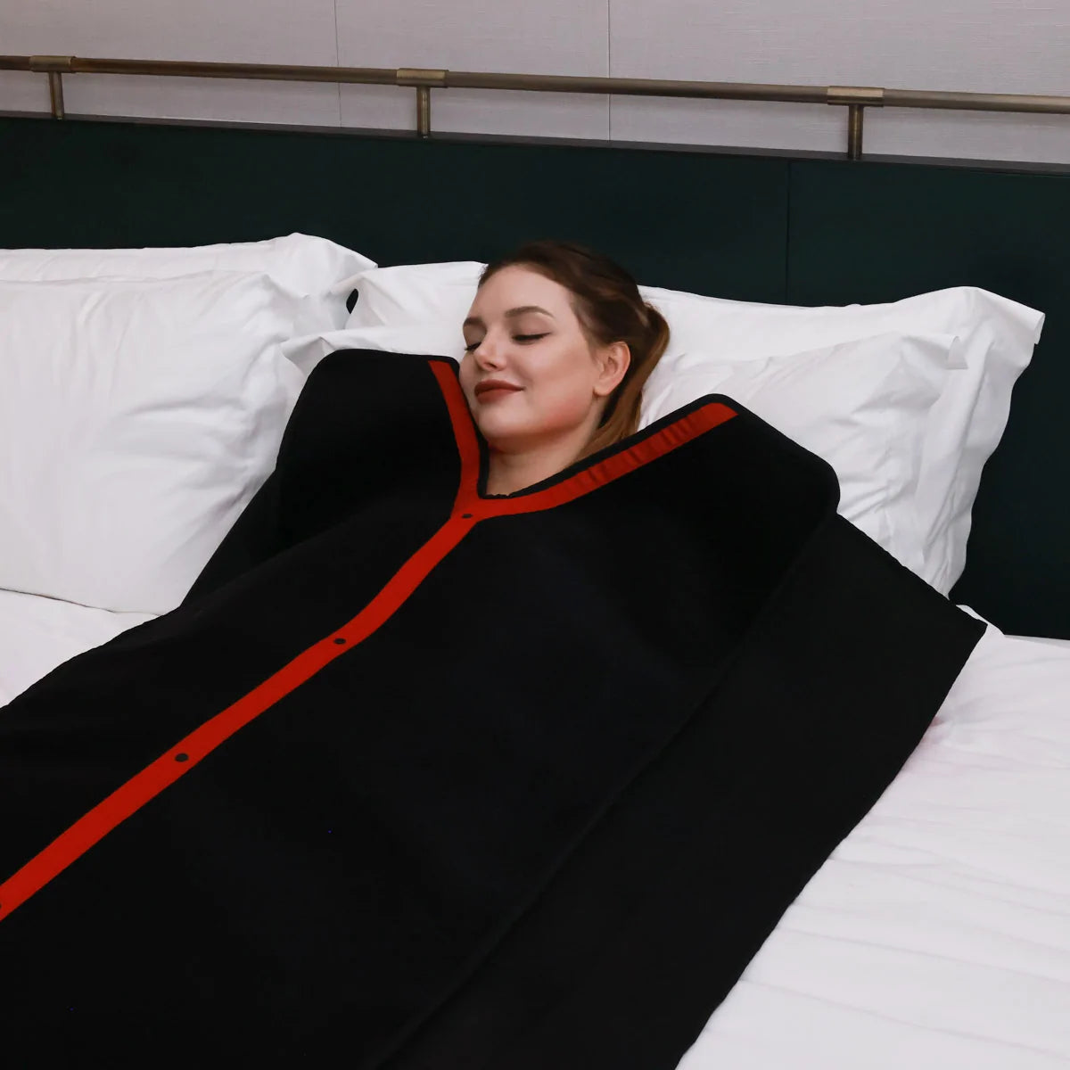 Woman lying on a bed wearing a black and red led therapy blanket.